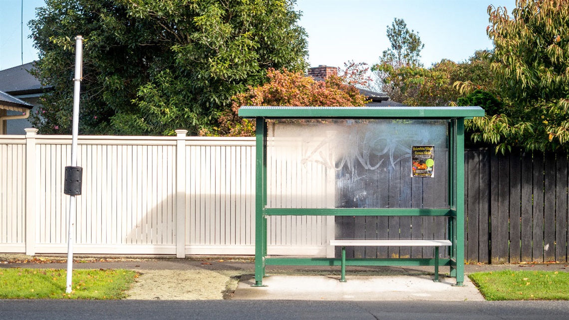Image shows a bus stop standing in front a white fence