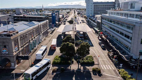 Image shows aerial view of buses entering the bus terminal on a wide city road.