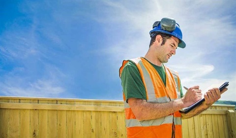 Inspector wearing safety gear making notes on a clipboard.