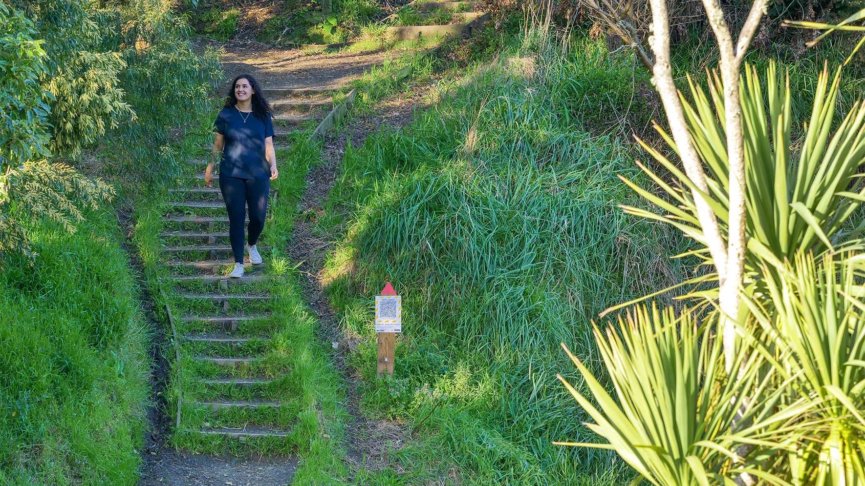 Young woman walking down steps cut into the side of a hill, with native bush on either side.