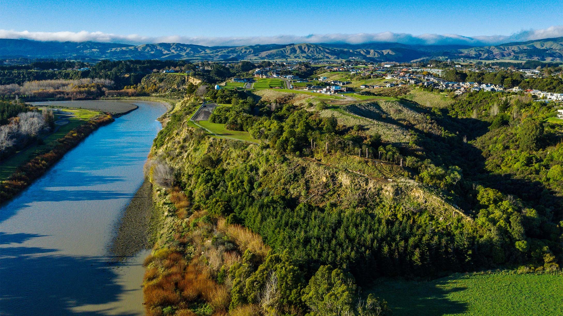 Aerial view of a heavily forested clifftop park overlooking the river.