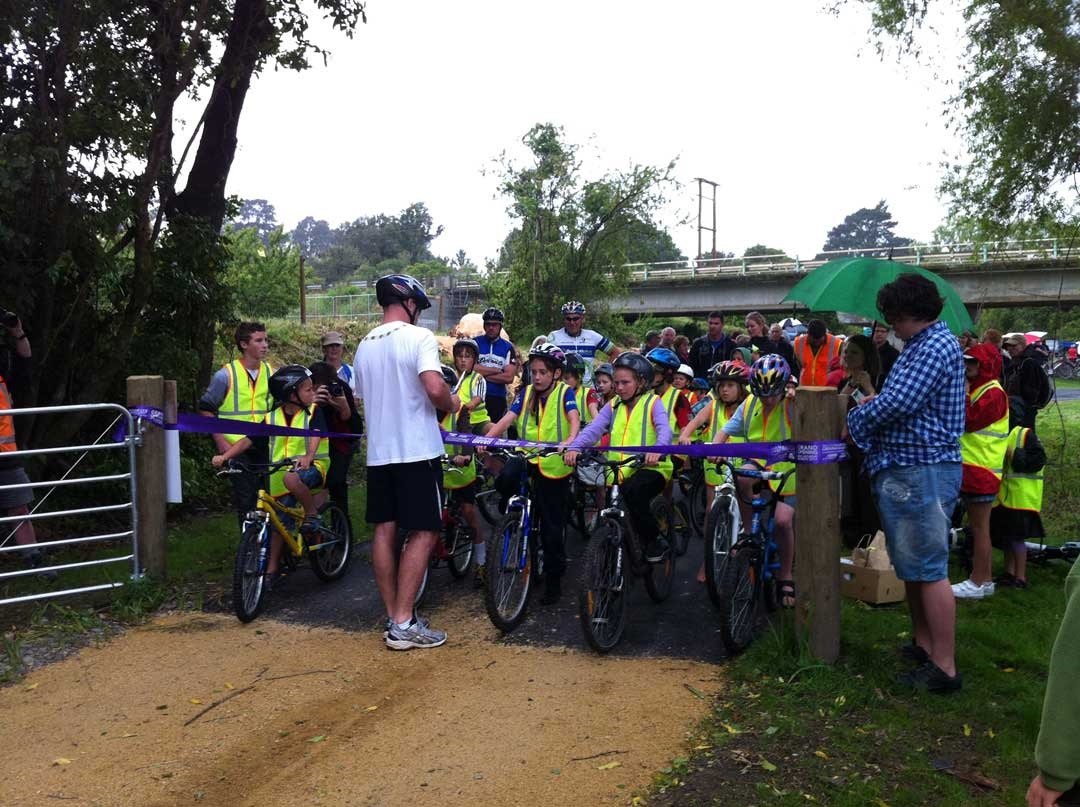 Photo shows man cutting a ribbon to open the new track with a group of primary school children on bikes waiting to use it.