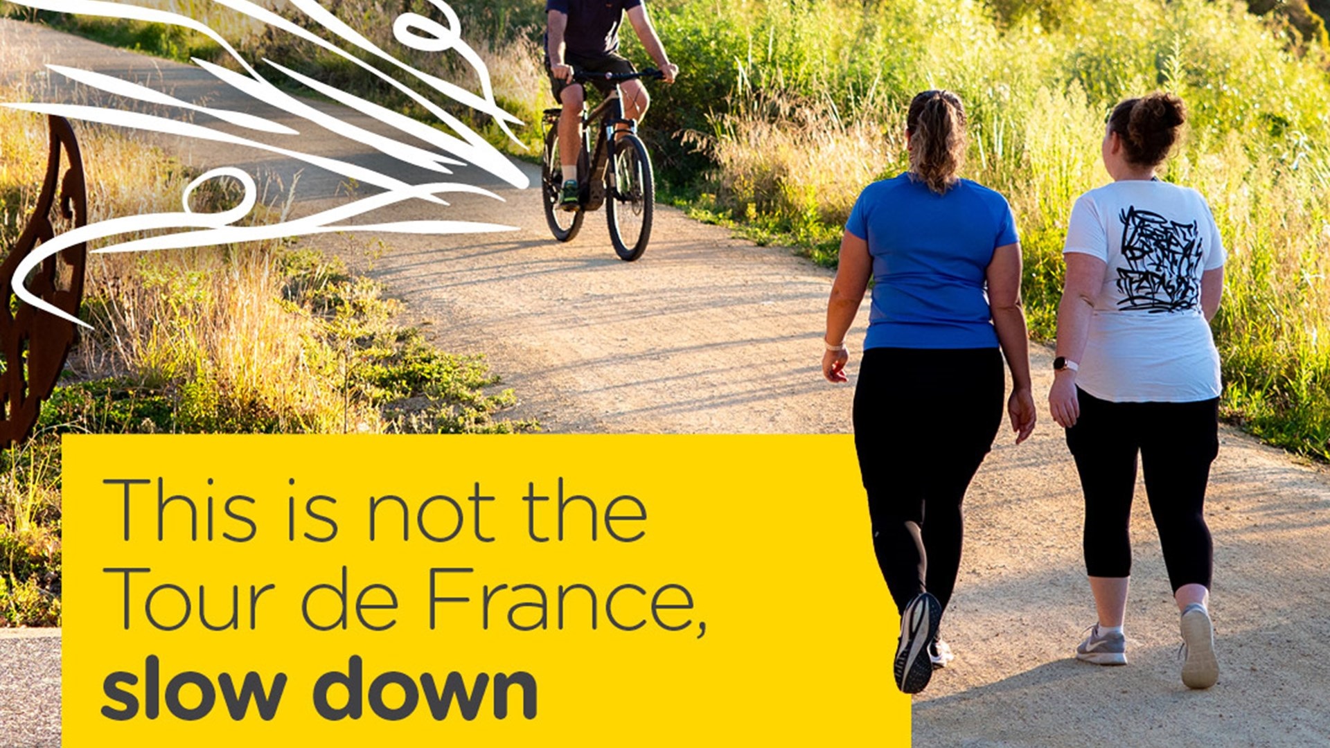 A person bikes towards 2 women walking on a shared pathway.