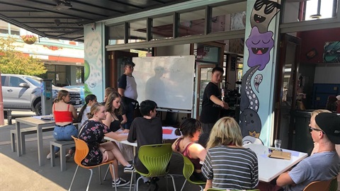 About a dozen teens relaxing at tables outside Youth Space.