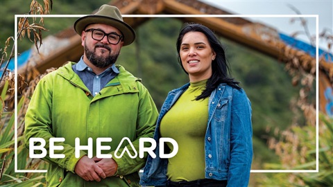 A couple stand in front of the whare at Te Apiti. Overlaid text reads 