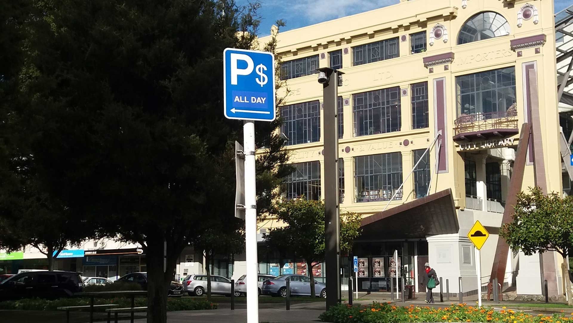 City street with parked cars and $P all day sign.