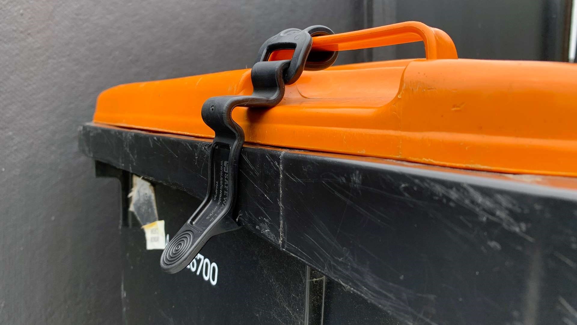 Photo shows closeup of a wheelie bin with the lid secured by a clip.
