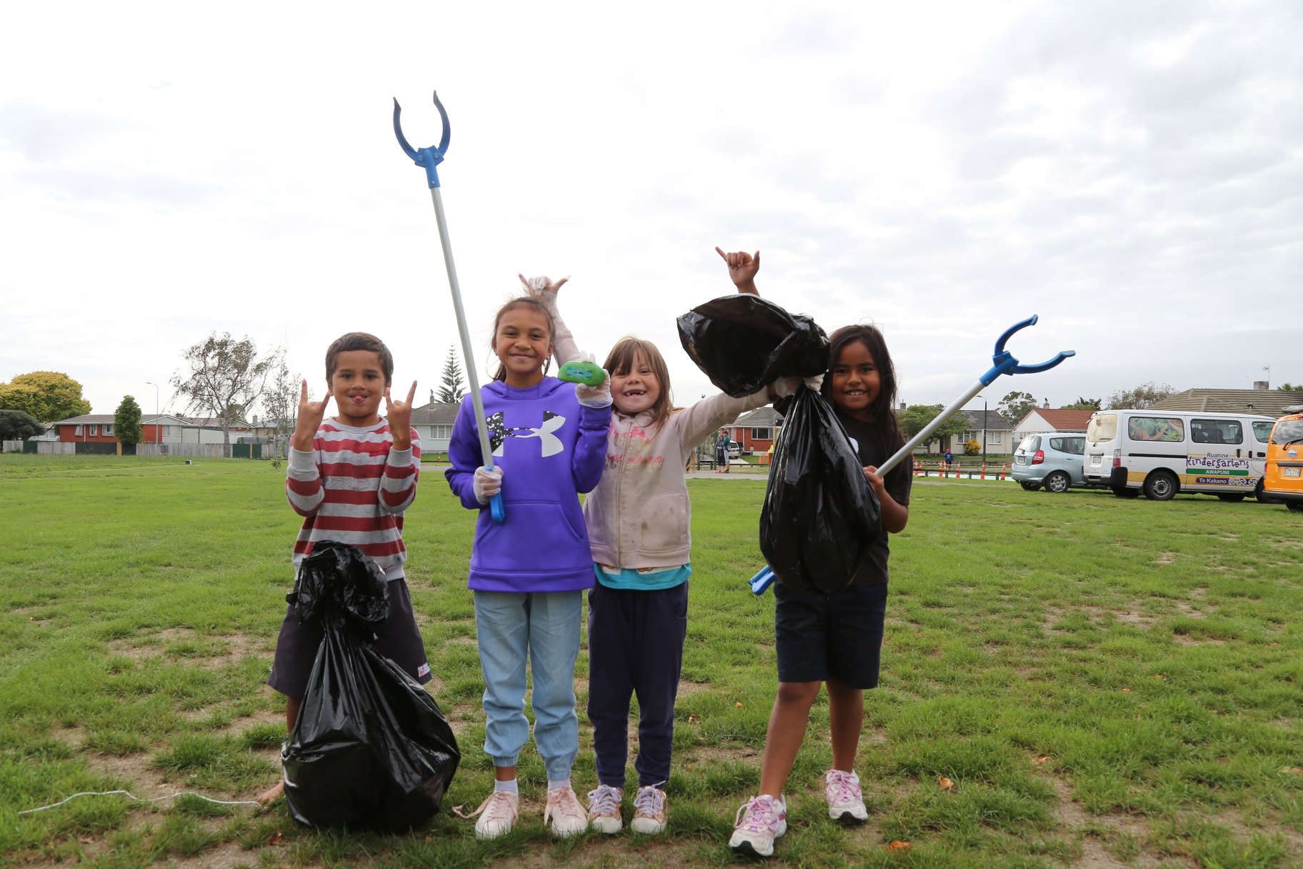 Photo shows kids with pick-up sticks and bags of rubbish at a community cleanup event in a park.