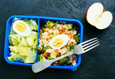 Photo shows lunchbox filled with salad and a metal fork resting on top of it.