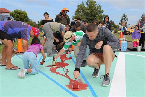Families painting a mural on the court of a local basketball court.