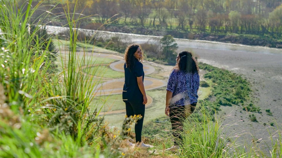 Photo shows two young women looking out at the splendid view of the river from the top of the steps at Anzac Park.