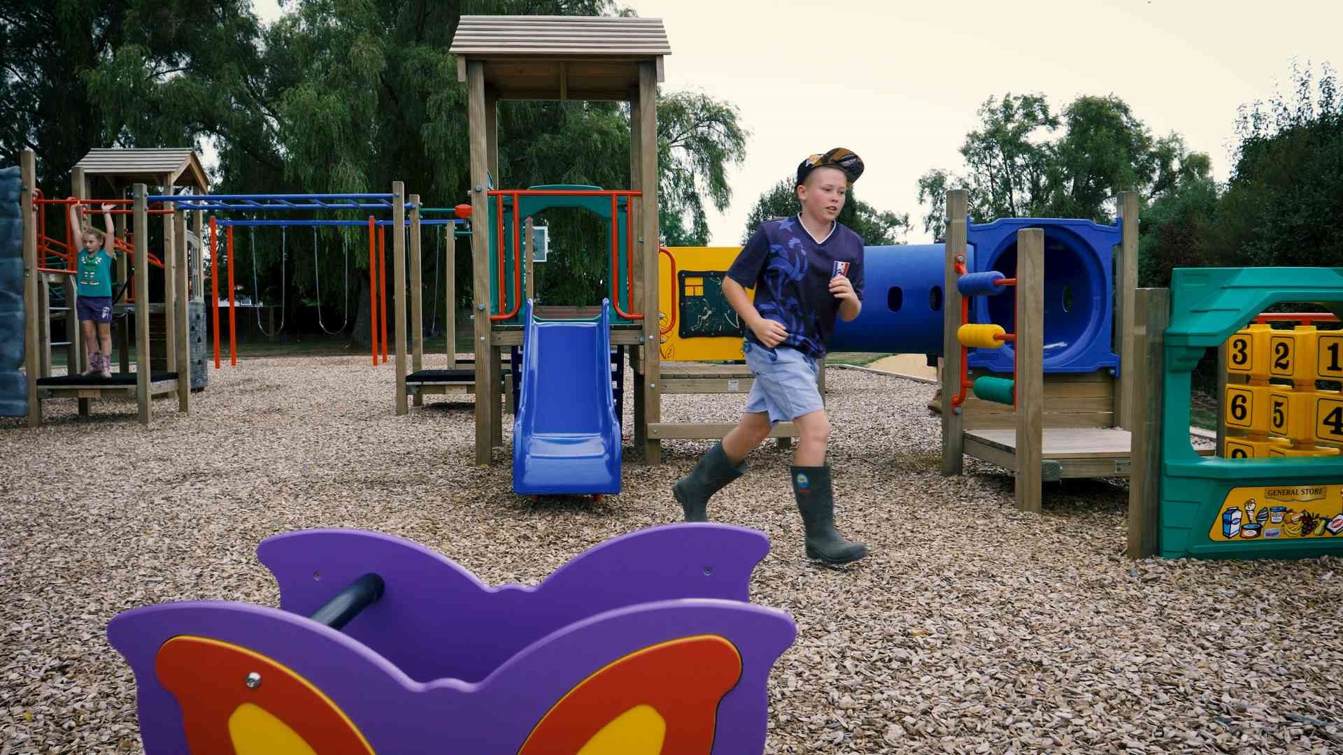 Photo shows children playing at Apollo Park. Playground equipment includes climbing frame, swings, slide, tunnel and counting blocks.