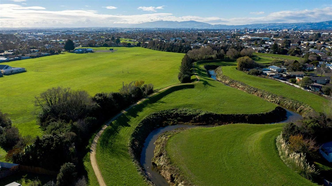 Photo shows large grassed area bordered by a stream and a limestone walkway.