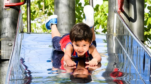 Photo shows gleeful child sliding headfirst down a shiny slide.