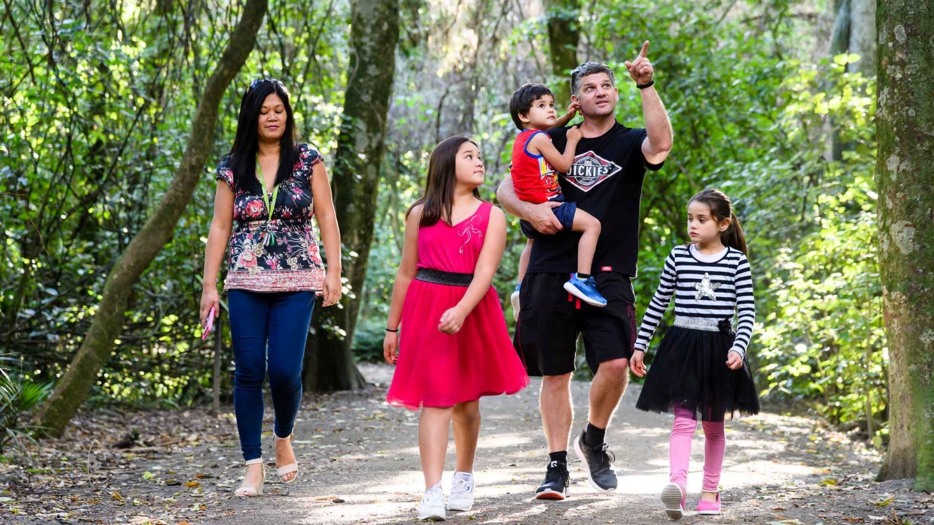 Photo shows family walking along on a limestone pathway underneath leafy trees.