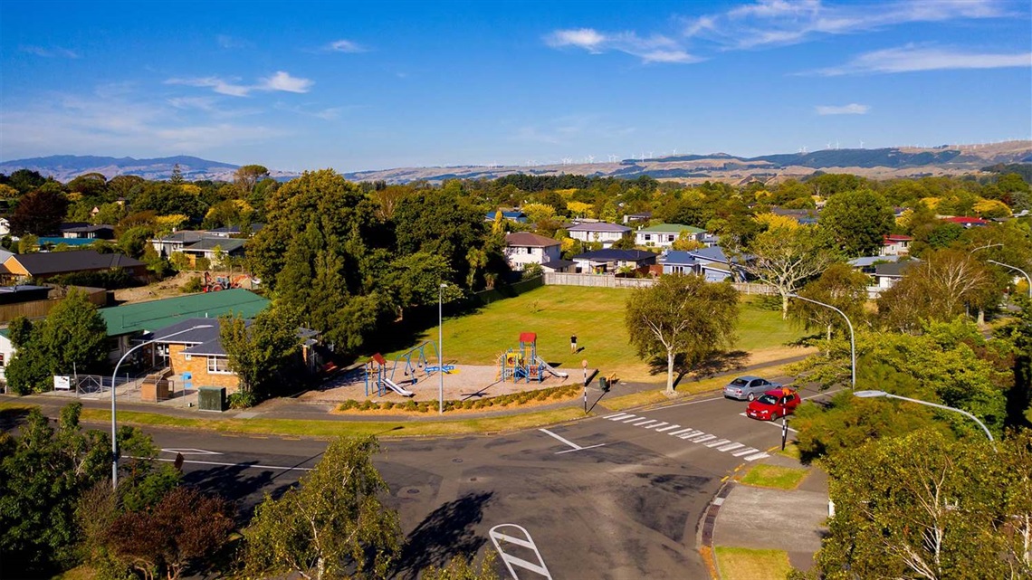 Photo shows small neighbourhood reserve with a playground and a grassed area for running around.