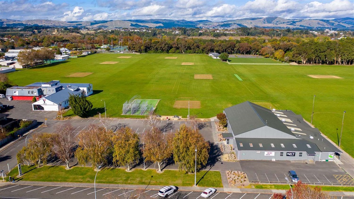Photo shows aerial view of sportsfields with a built facility and carpark in the foreground and the Esplanade trees in the background.