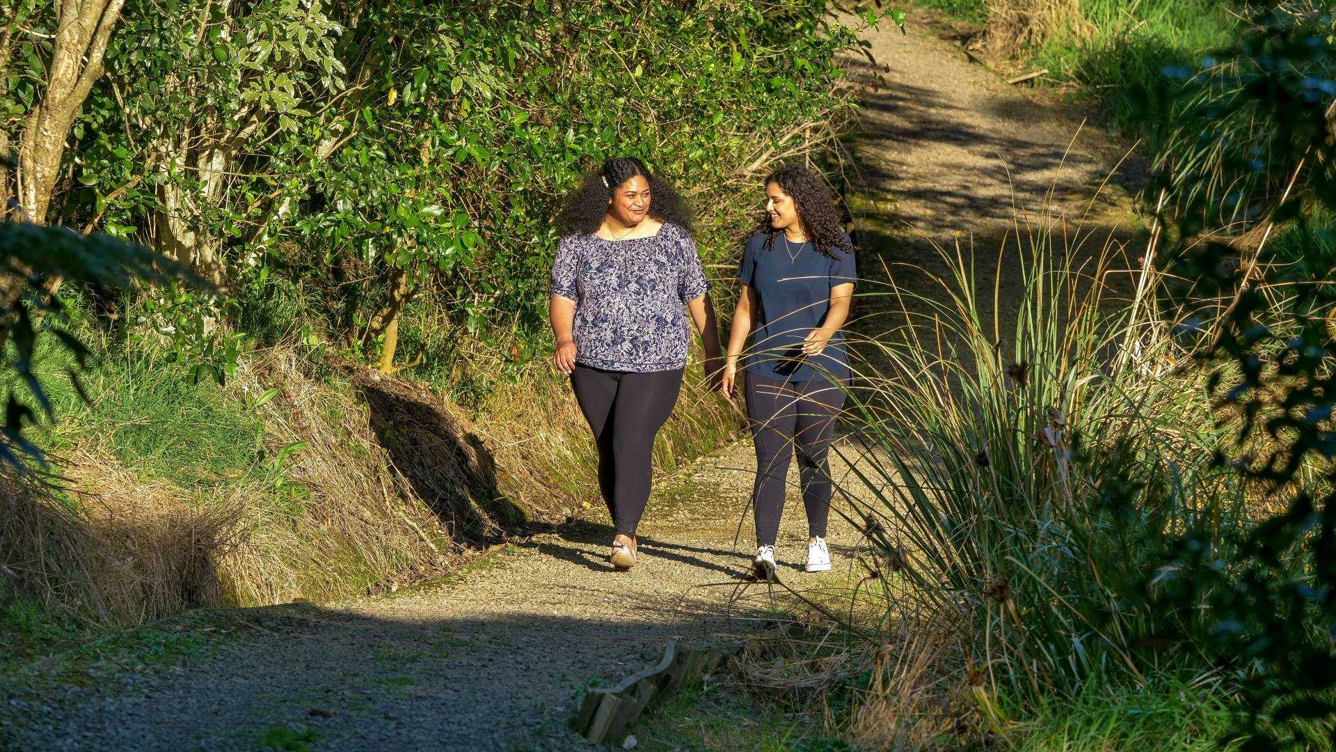 Photo shows two young women talking as they walk along a gravel path which is rising steeply out of a bushy valley.