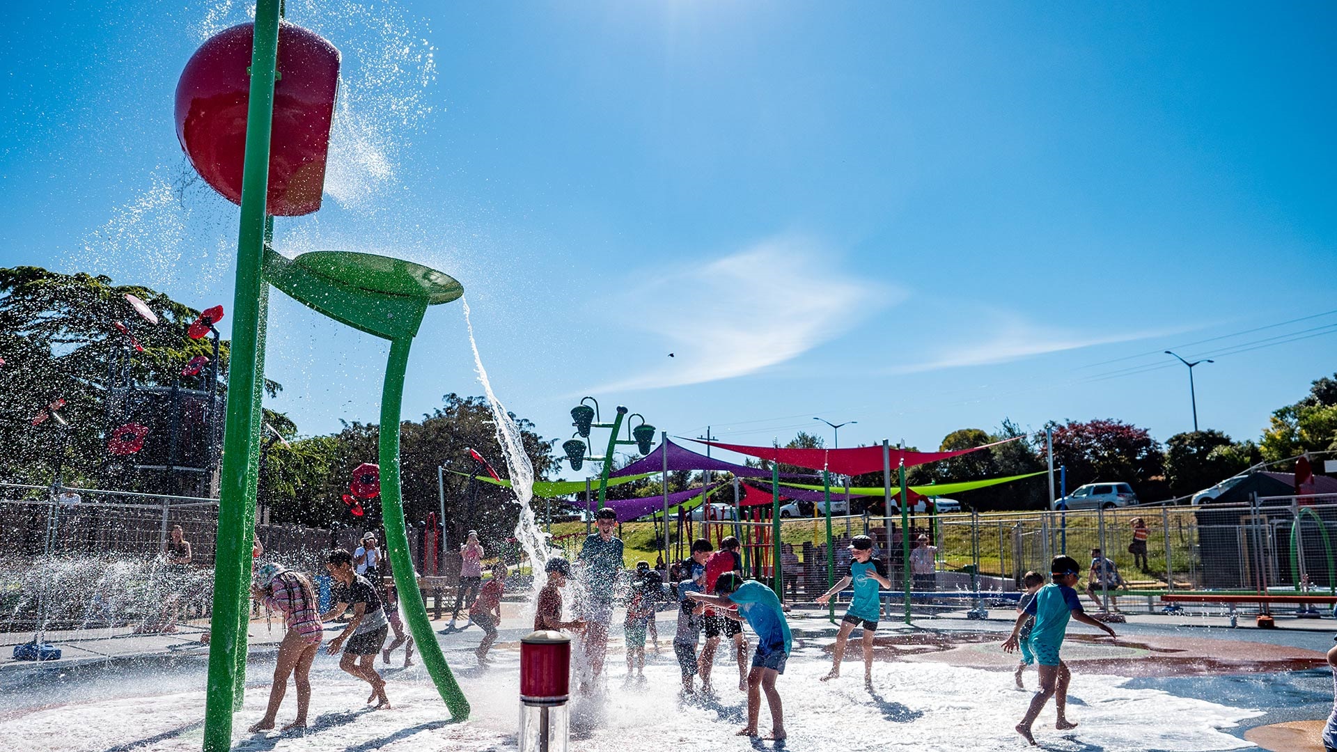 The image shows children playing at the splashpad under the sun.
