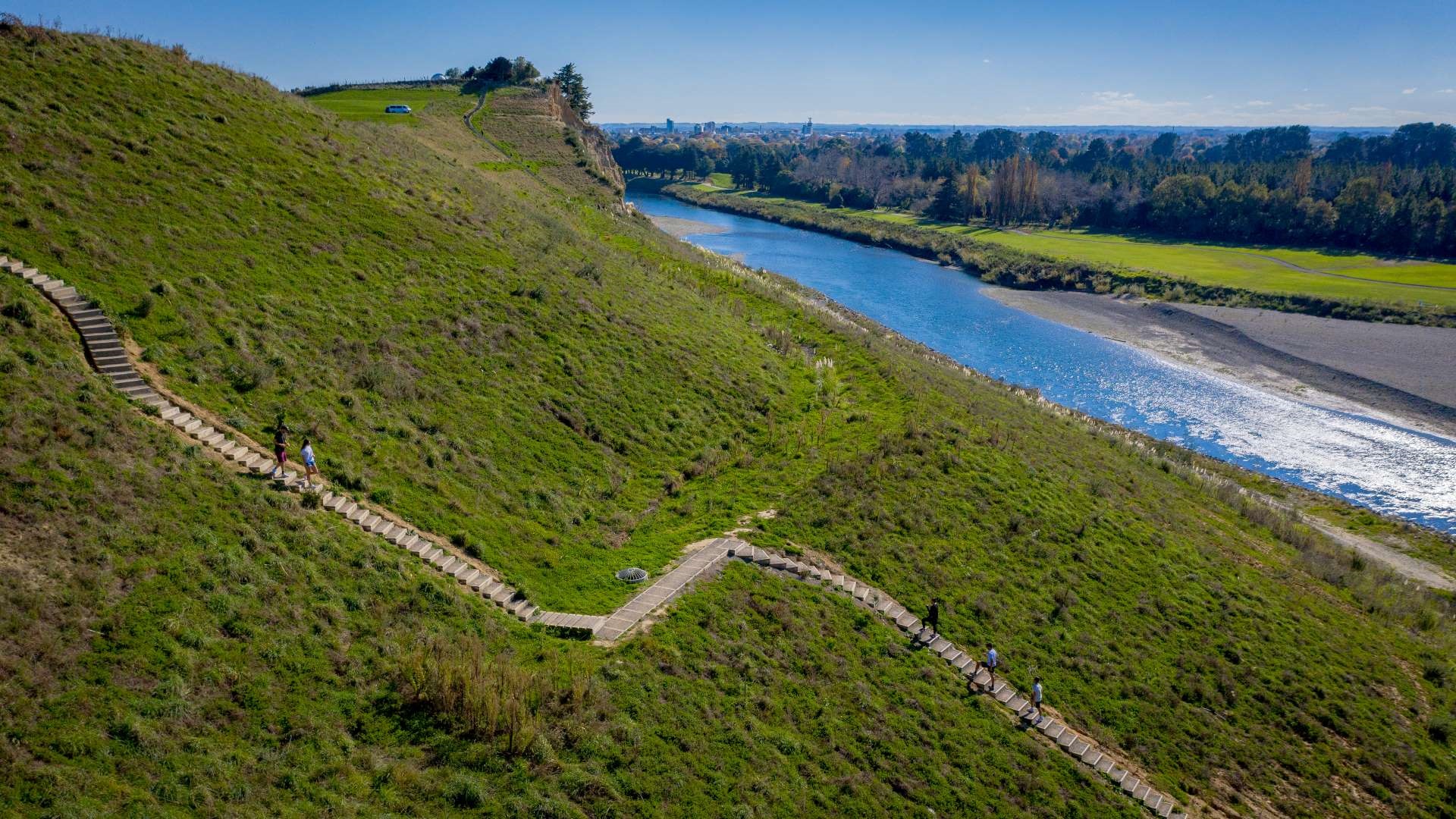 Photo shows people climbing steep steps zigzagging up a hillside on the bank of the Manawatū River.