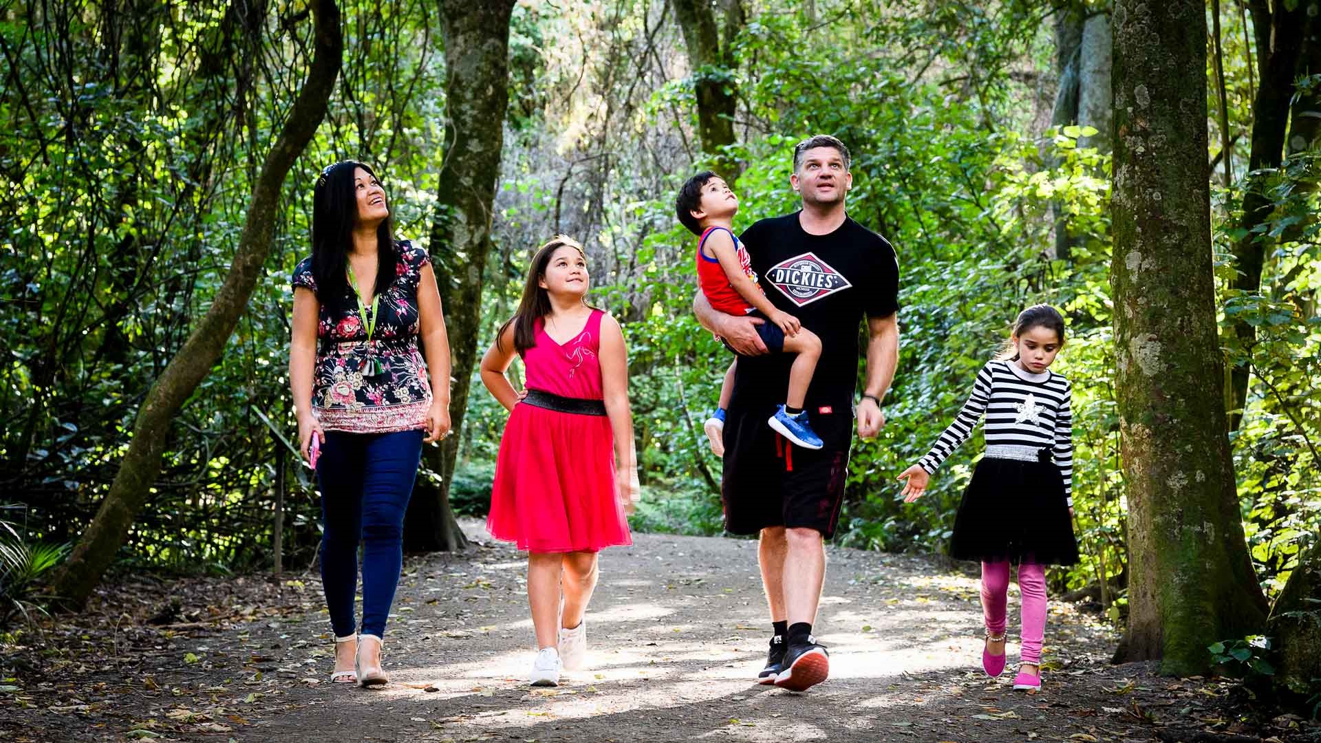 Photo shows family walking along on a limestone pathway underneath leafy trees.