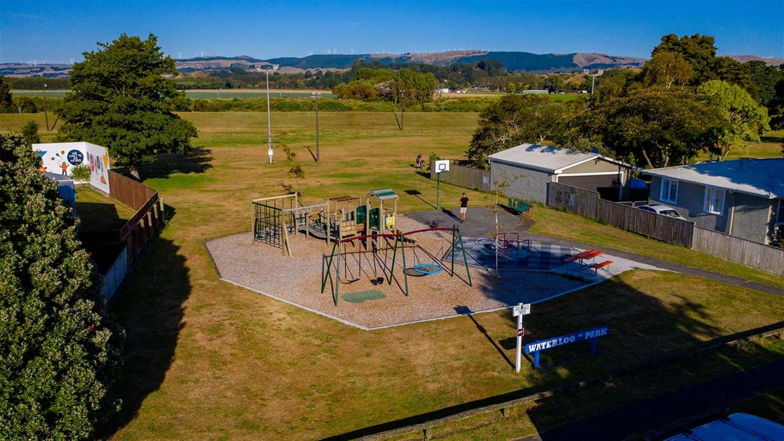 Photo shows a small park with a children's playground and basketball hoop, which opens up on to the Manawatū River shared pathway.