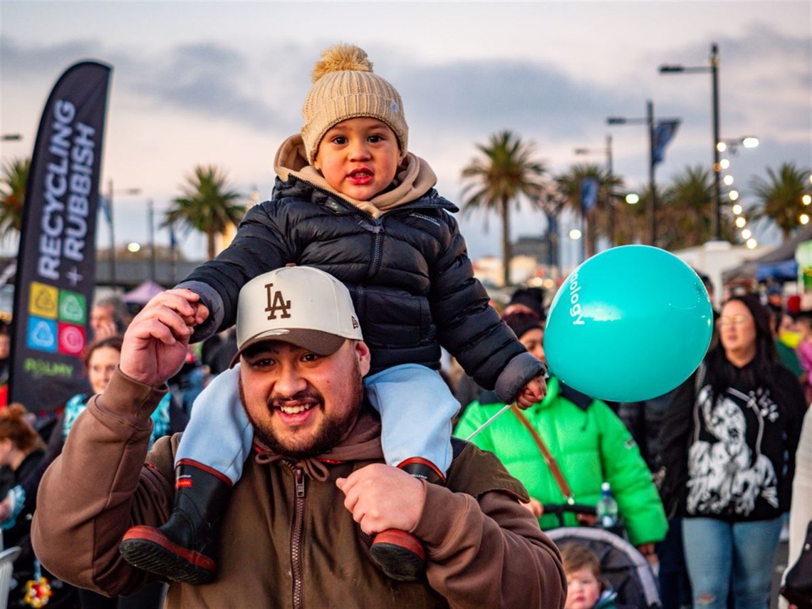 A young child carrying a balloon rides on their father's shoulders.