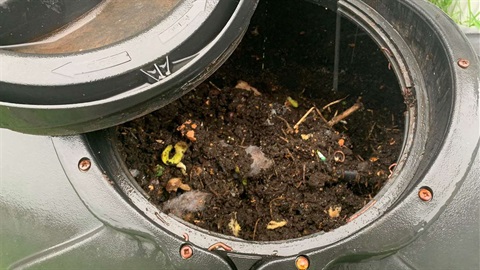 Photo shows rotator compost bin with the lid off and the compost visible inside.
