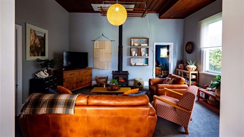 Photo shows a colourful lounge with plants and an eclectic array of op-shopped treasures, including comfy seating and collectable mid-century ceramics and glass. 