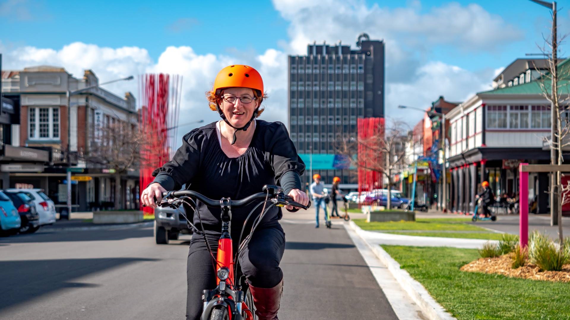 Photo shows woman in regular clothes riding a step-through bike along Cuba Street with people on e-scooters in the background.