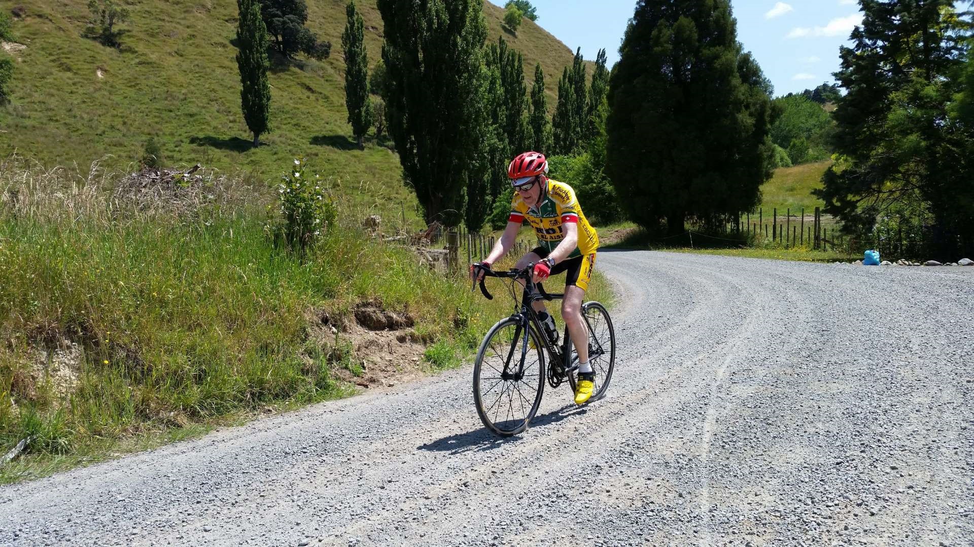Photo shows man in lycra riding a racing bike along a gravel road in the countryside.