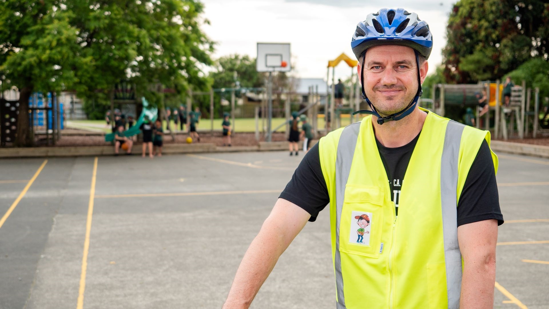 Photo shows man in hi vis vest and helmet in school playground.