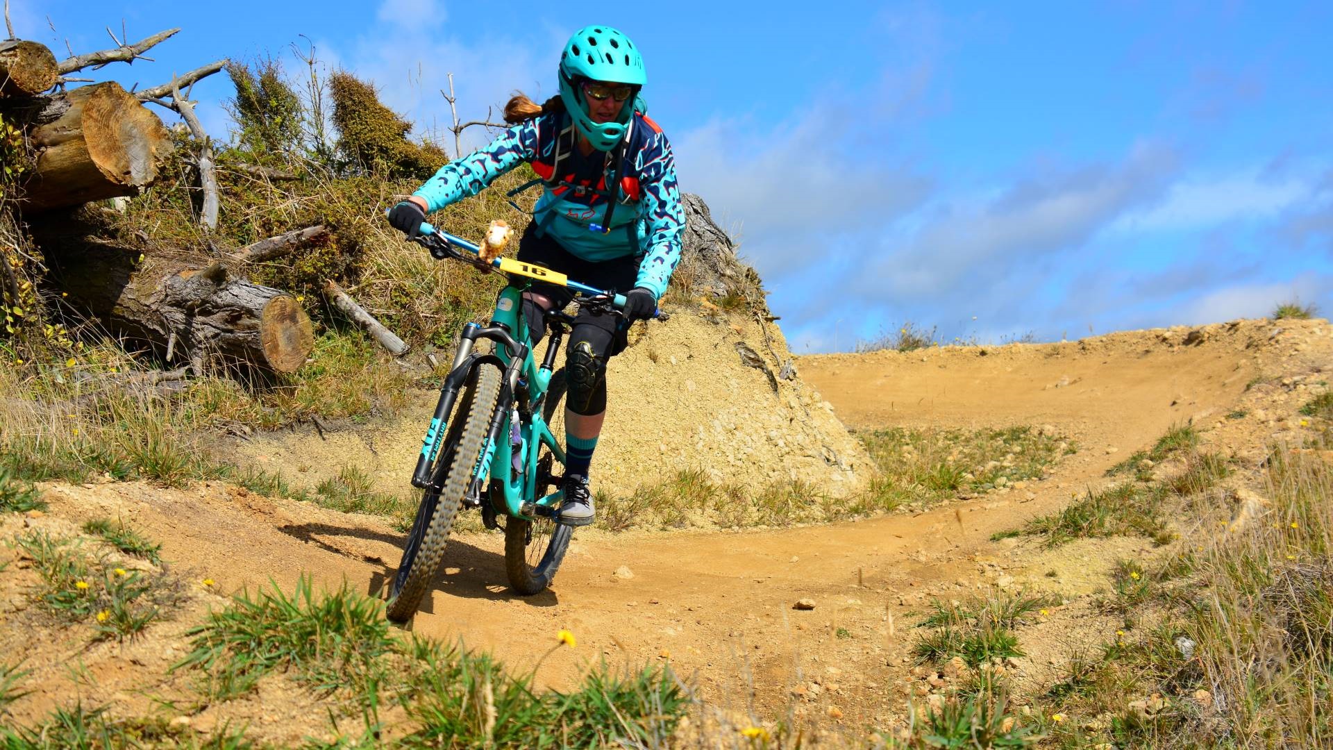 Photo shows woman with full helmet and protective gear riding a mountainbike on a downhill dirt track.