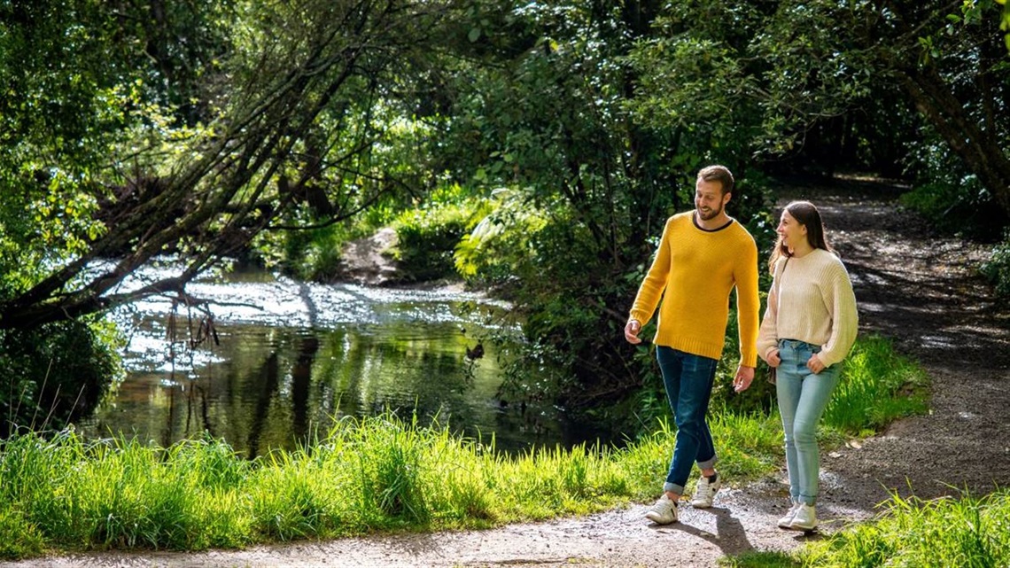 Couple strolling along a shady pathway alongside Turitea Stream.