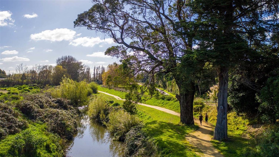 Photo shows people walking along a limestone pathway meandering alongside a stream and riparian planting.