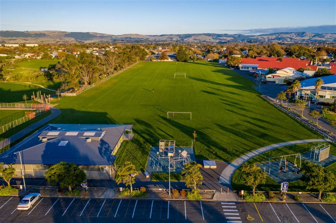 Aerial view of sportsfields and a small playground neighboured by a reserve, a large car park, and Freyberg swimming pool.