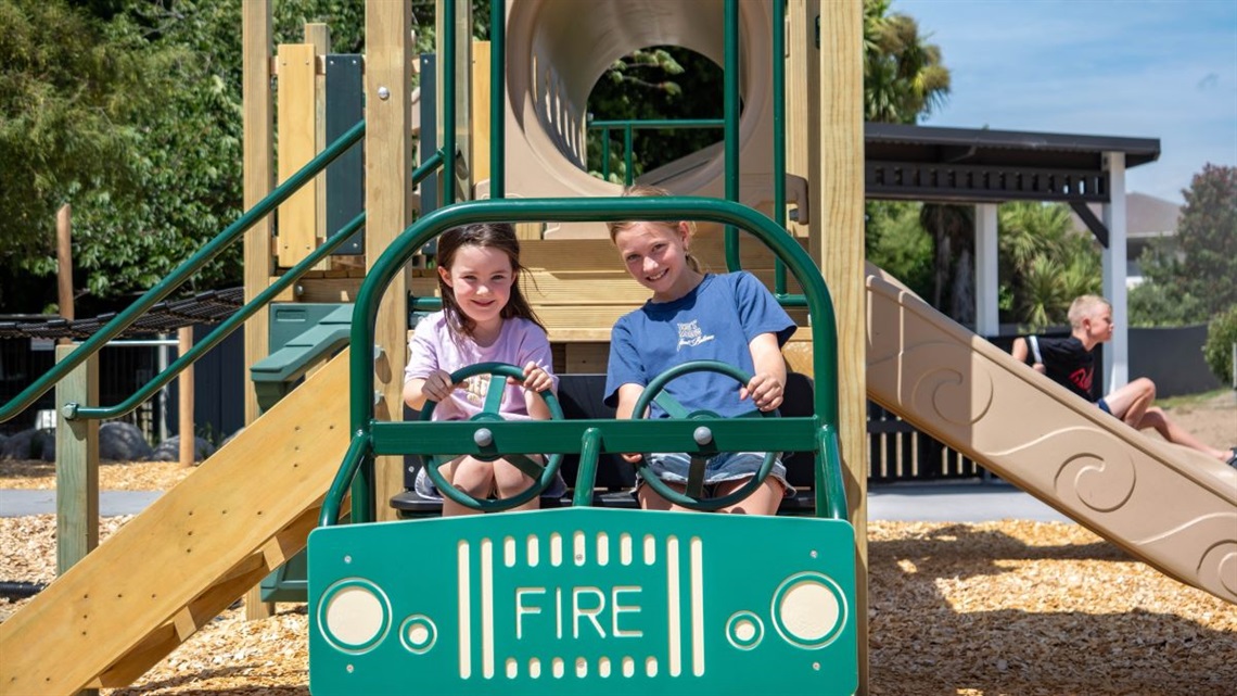Two girls playing on the fire-truck feature that's part of the new playground at Franklin Reserve.